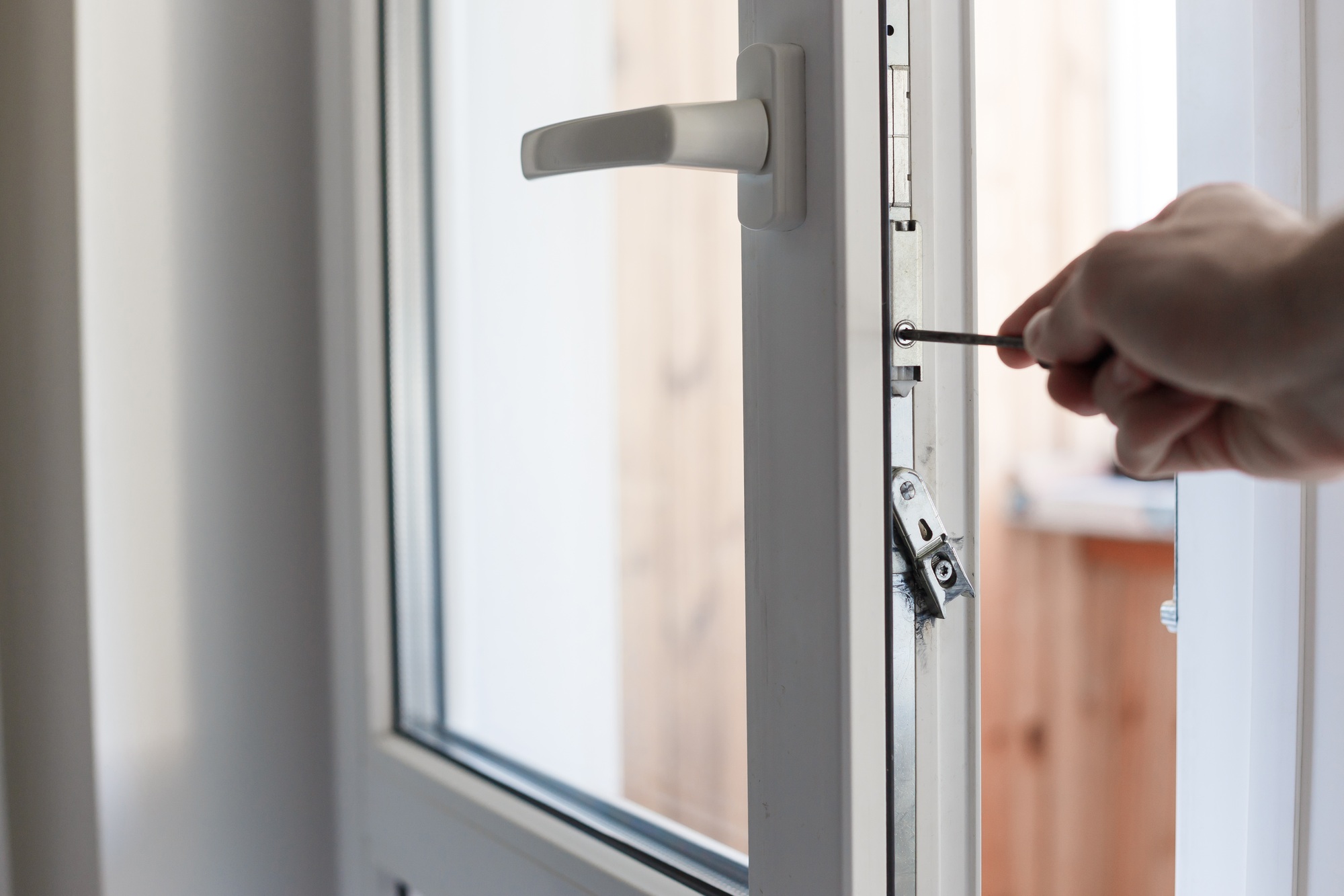 Man's hand uses screwdriver for adjustment of hardware of the uPVC door mechanism.